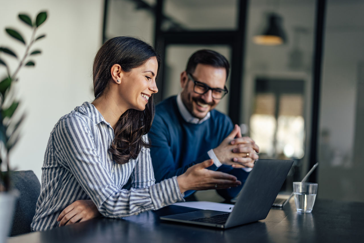 A smiling business man and woman sitting near a laptop
