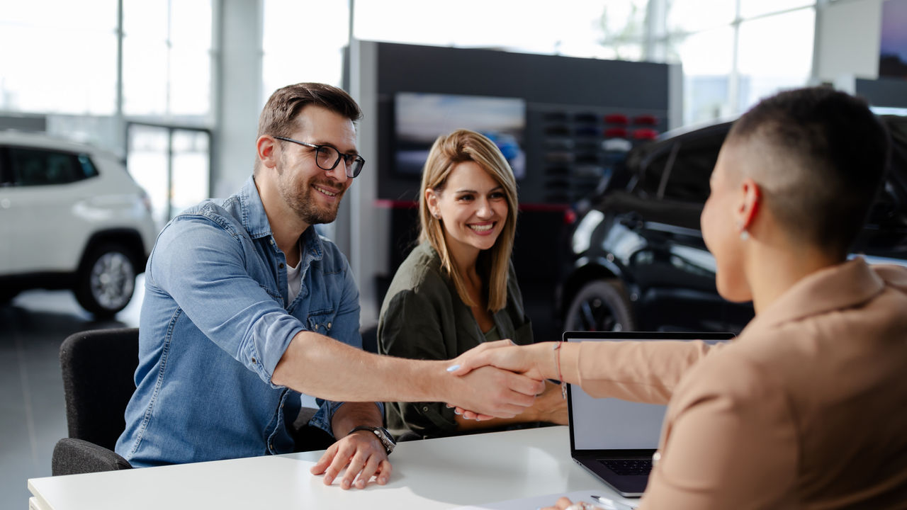 Male customer and female car dealer shaking hands at showroom.